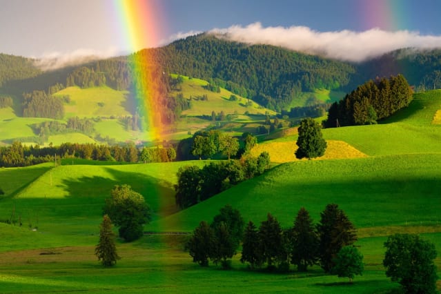 Image of a rainbow against green hills and trees.